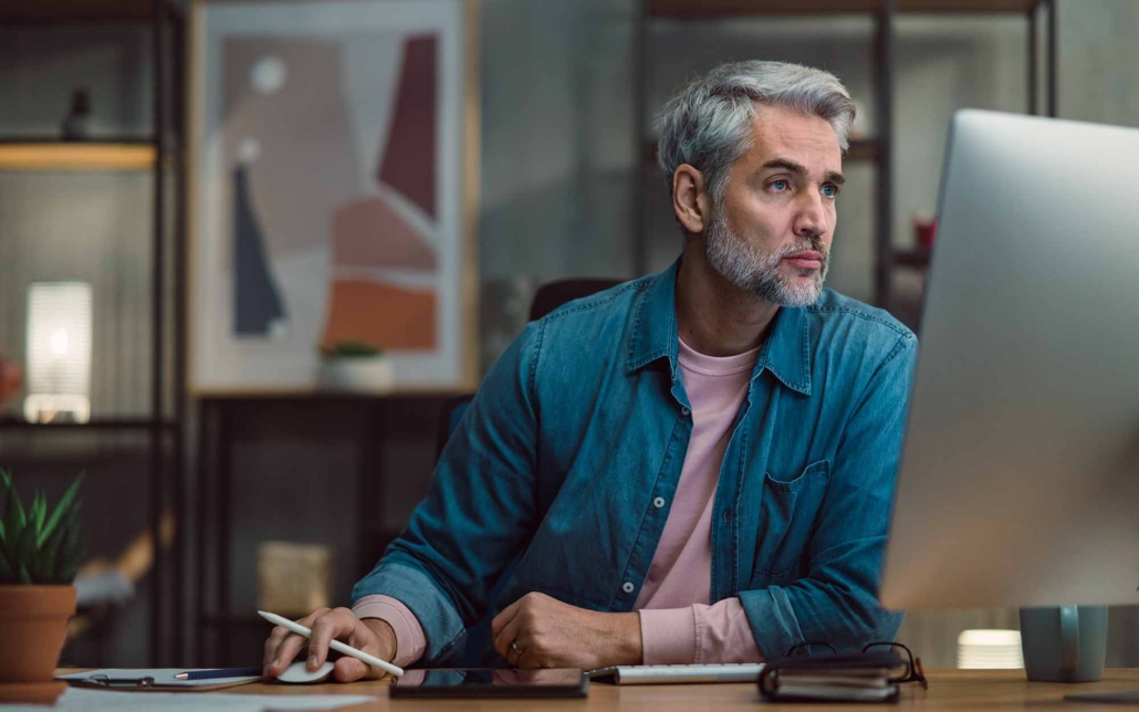 Mature man architect working on computer at desk indoors in office_