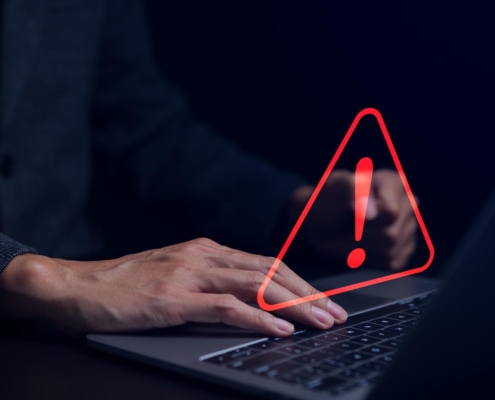 Side view of a man typing on a laptop with a red warning graphic hovering above the keyboard