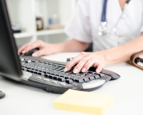 Side view of a physician with a stethoscope around her neck typing on a keyboard