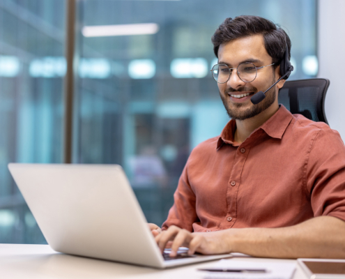 Smiling professional wearing headset working on laptop in modern office