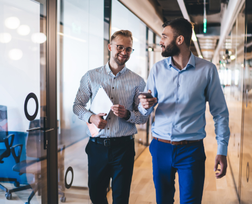 Positive male entrepreneurs in smart casual wear strolling in office